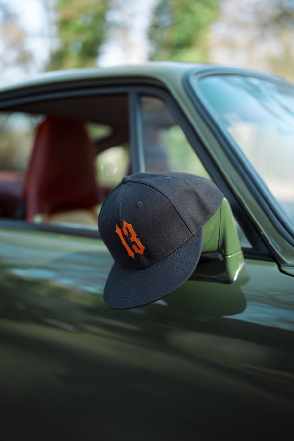 Casquette noire au chiffre 13 orange posée sur le rétroviseur d'une voiture ancienne verte.