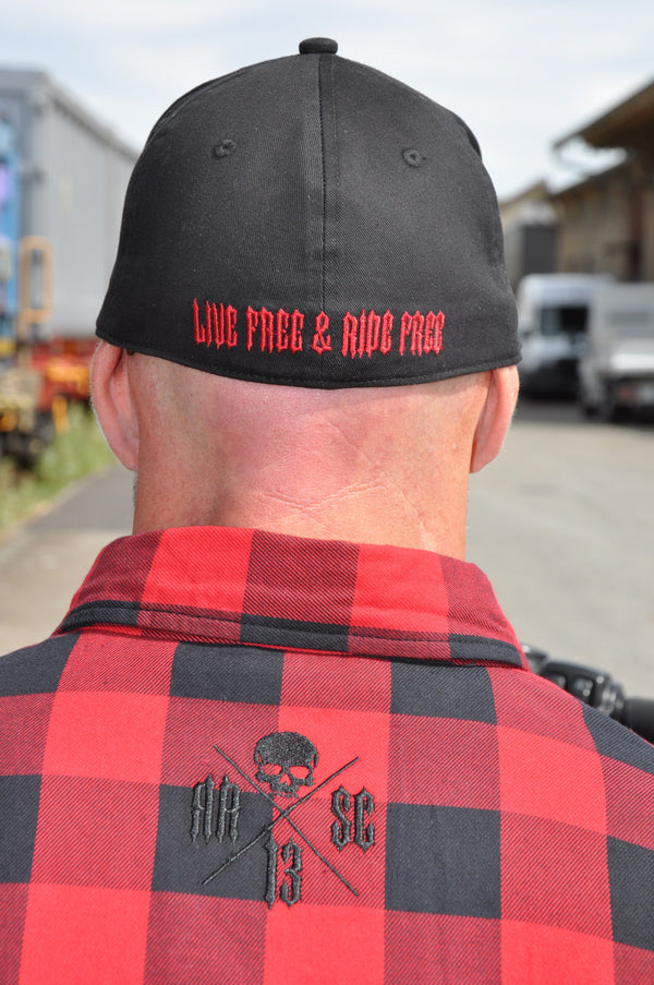 Gros plan de dos : casquette noire brodée Live free & ride free en rouge et col d'une chemise flanelle rouge au logo crâne brodé.